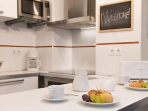 Une cuisine moderne agrémentée d’un panneau d’accueil, d’une machine à café, d’une carafe et d’une assiette garnie de viennoiseries et de raisins.
