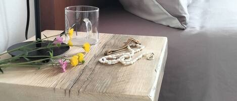 Una mesita de noche de madera con una lámpara, un vaso, un collar y flores.