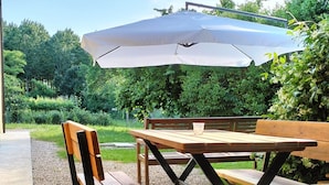 A wooden picnic table with a bench under a covered area, surrounded by greenery. - Agriturismo Le Crede 1930  (Portogruaro)