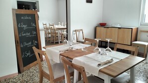 A dining area with wooden tables and chairs, a chalkboard menu, and a kitchen area in the background. - Agriturismo Le Crede 1930  (Portogruaro)