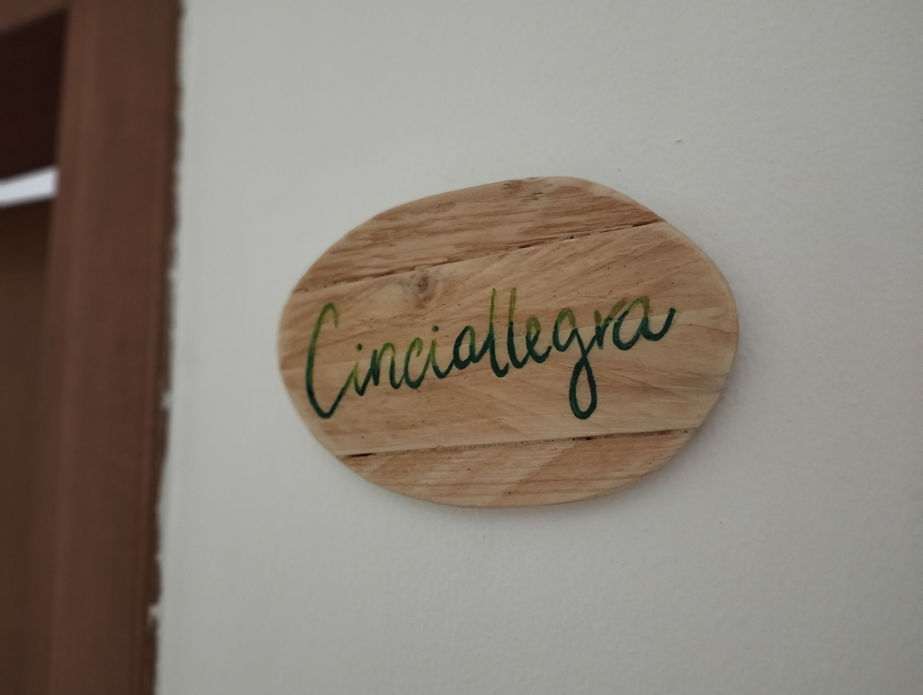 A circular wooden sign with the text "Cinciallegra" on a white wall.
