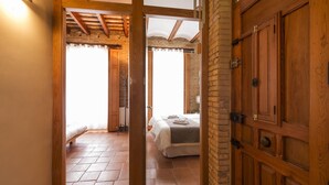 Een smalle gang die leidt naar een slaapkamer met een bed, een houten deur en een bakstenen muur.