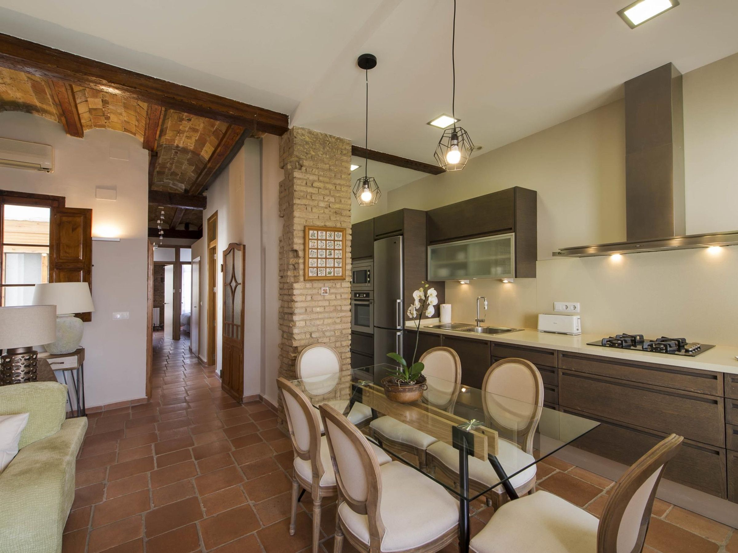 A modern kitchen with a dining area, featuring a stone wall, wooden beams, and contemporary appliances.