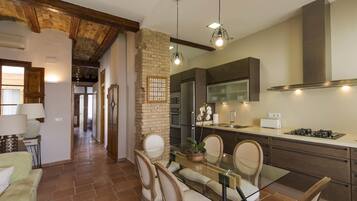 A modern kitchen with a dining area, featuring a stone wall, wooden beams, and contemporary appliances.