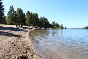 A sandy beach with clear water, trees, and a picnic table.