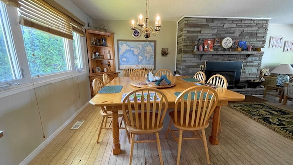 Un comedor con una mesa y sillas de madera, una chimenea, un mapa mundial en la pared y una estantería.