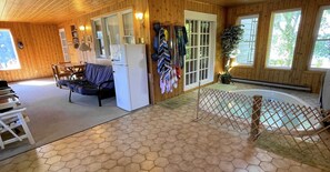 A wooden cabin interior with a dining area, a sofa, a refrigerator, and a view of the outdoors through large windows. - Charming Lakeside Retreat: Cozy and Convenient on Chemong Lake (Lakefield)