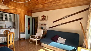 A cozy living room with a sofa, a chair, and a dining area with a table and chairs. - Charming 2-Room Apartment for 4 near Lifts - Alpe d'Huez (Huez)