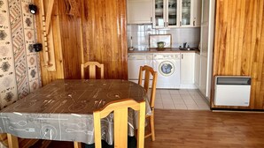 A wooden interior with a dining table, chairs, a washing machine, and a small kitchen area. - Charming 2-Room Apartment for 4 near Lifts - Alpe d'Huez (Huez)