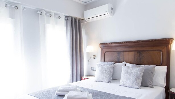 Ein Hotelzimmer mit einem großen Bett, grauer Bettwäsche, einem Holzkopfteil und einer Klimaanlage an der Wand.