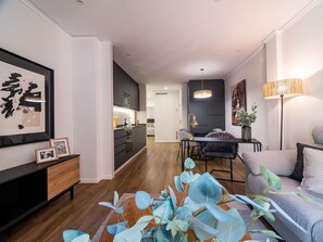 Uma sala de estar moderna com um sofá, uma mesa de jantar e uma cozinha ao fundo.