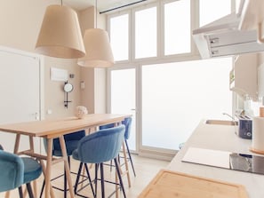 Cozinha moderna com mesa de madeira, cadeiras azuis e luminárias pendentes.