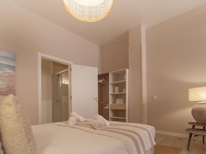 Quarto com cama, guarda-roupa, banheiro com porta de vidro e luminária.