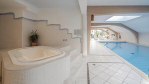 A swimming pool area with a hot tub, tiled flooring, and a view of the pool.