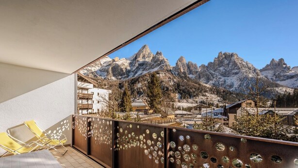 A balcony with a view of snow-capped mountains, a chair, and a decorative metal fence.