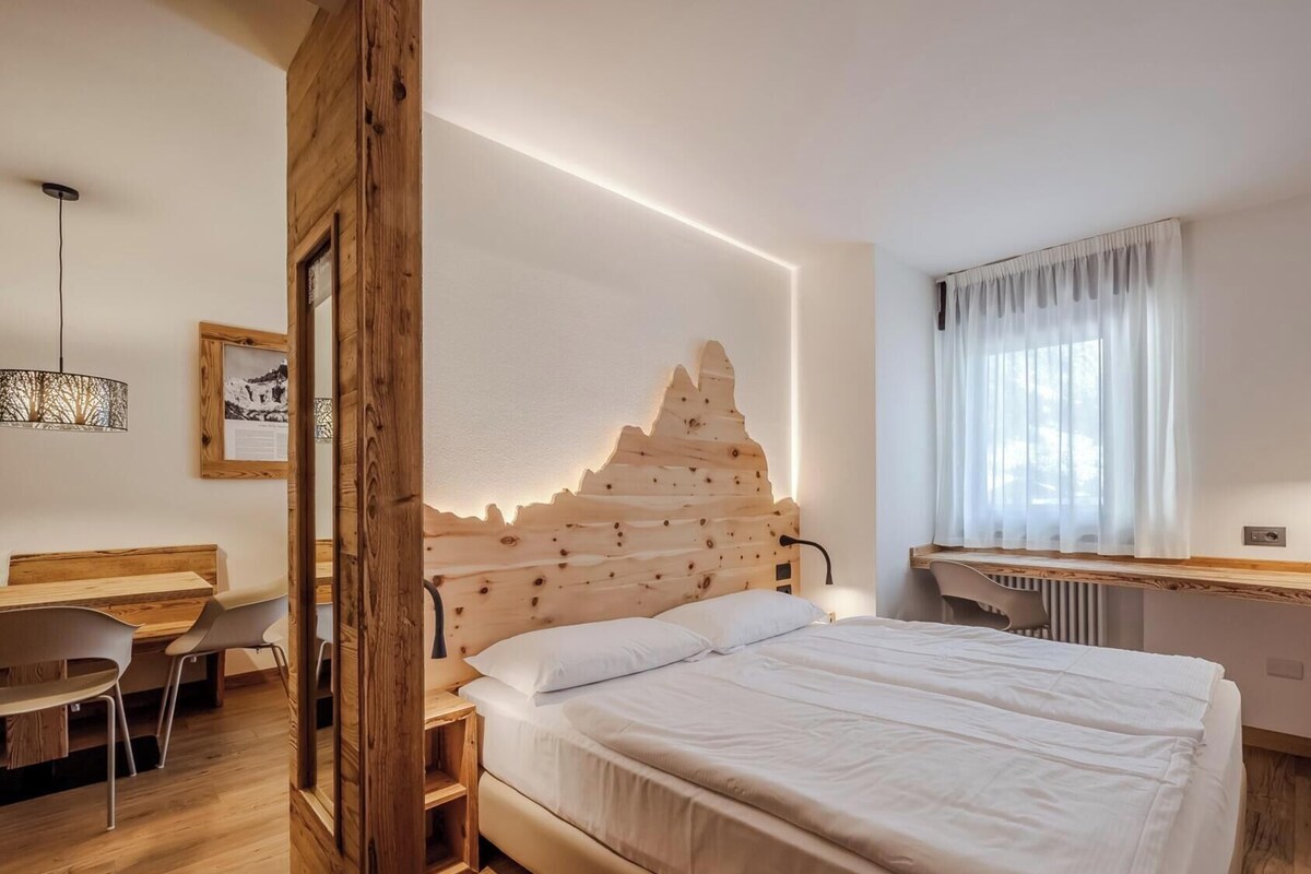 A bedroom with a wooden headboard, a bed, a desk, and a chair.