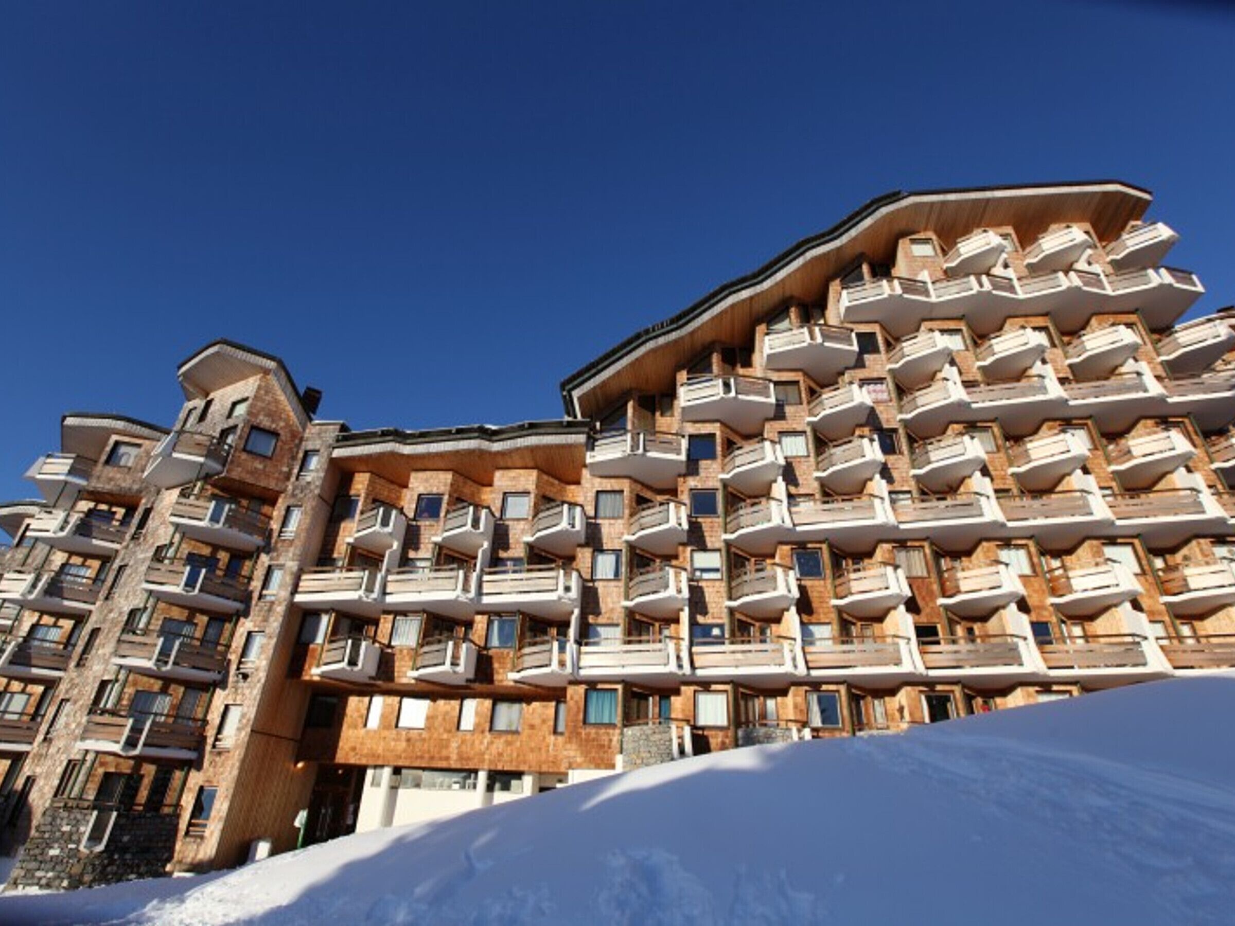 A multi-story hotel with balconies and a ski slope in the foreground.