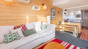 A modern living room with a white sofa, a wooden dining table, and a kitchen in the background. - Cozy 2-room apartment in Avoriaz with fireplace, south-facing balcony (Avoriaz)
