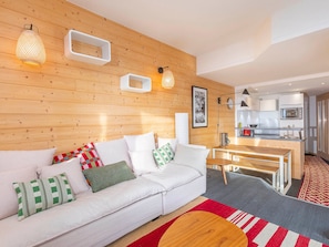 Ein modernes Wohnzimmer mit einem weißen Sofa, einem Holzesstisch und einer Küche im Hintergrund.