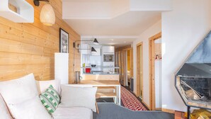 A modern living room with a wooden wall, a sofa with cushions, a fireplace, and a kitchen in the background. - Cozy 2-room apartment in Avoriaz with fireplace, south-facing balcony (Avoriaz)