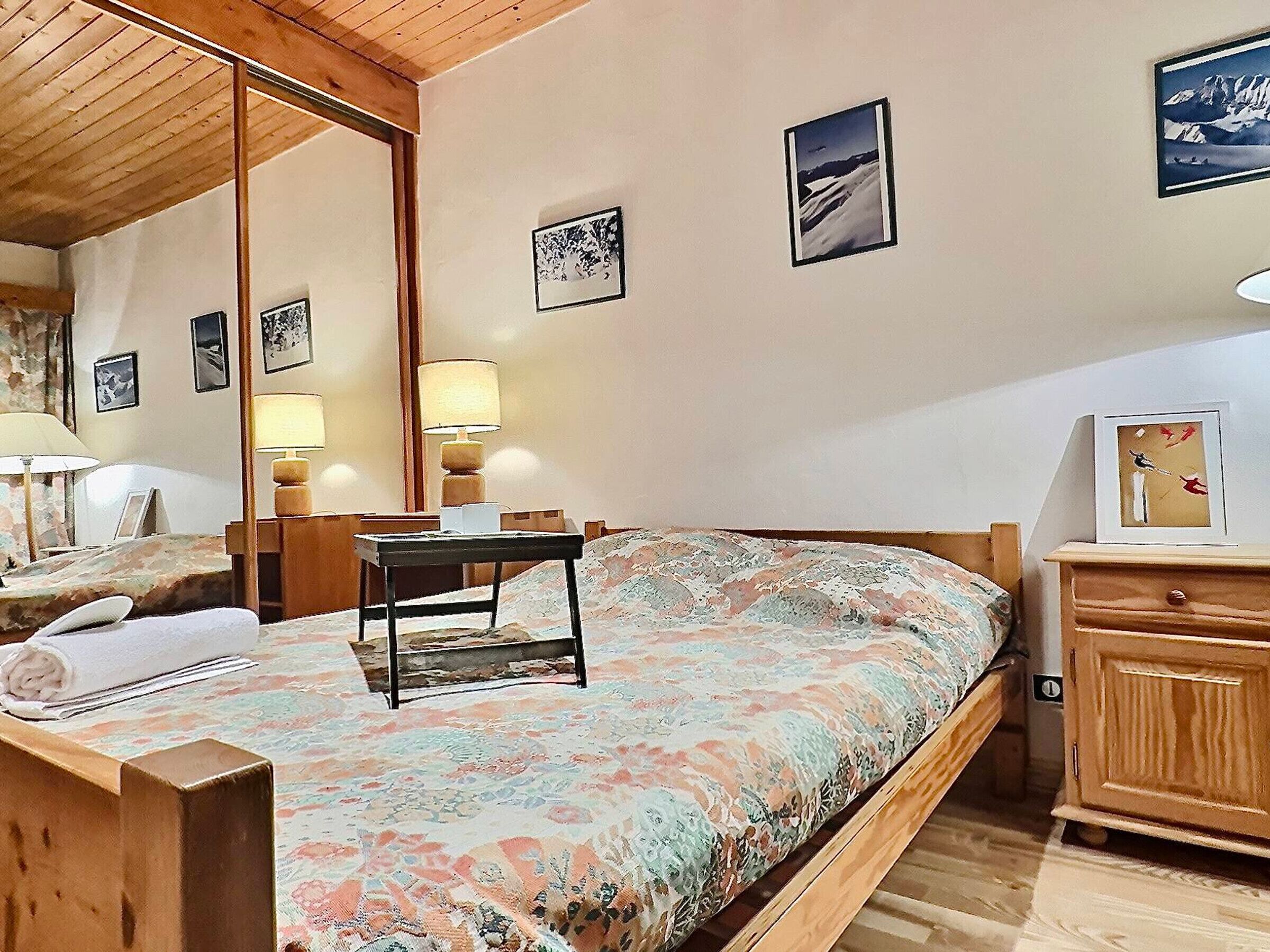 A bedroom with a bed, bedside tables, lamps, and framed pictures on the wall.