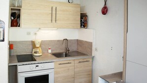 Een kleine keuken met houten kastjes, een inbouwoven, een spoelbak en een koffiezetapparaat.