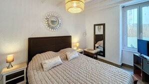 A bedroom with a large bed, bedside lamps, a decorative mirror, and a ceiling light fixture.