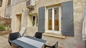 An outdoor patio with a table and chairs, a window with shutters, and a potted plant.