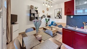 A modern living room with a dining area, red kitchen cabinets, and a mounted TV.