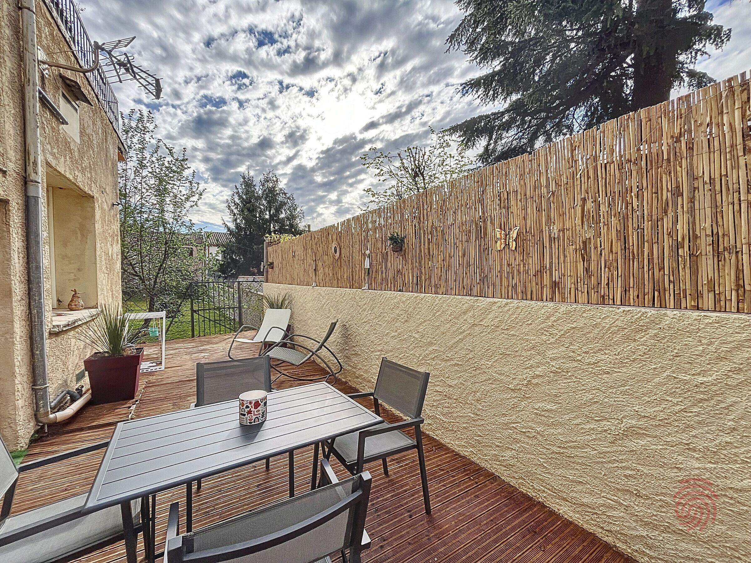 Eine Terrasse im Freien mit Tisch und Stühlen, einem Holzzaun und Blick auf die Umgebung.