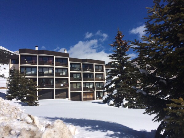 Hotel com vários andares e varandas, rodeado por neve no chão e nas árvores.