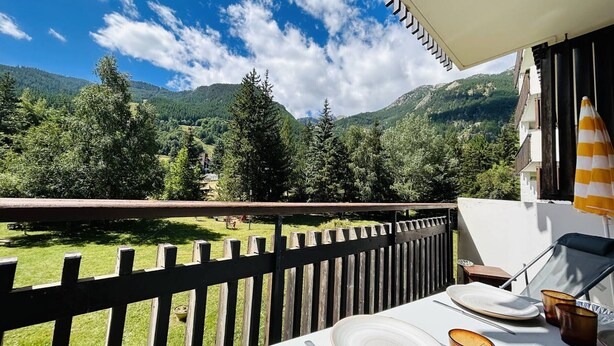 A balcony with a table set for dining, overlooking a mountainous landscape.