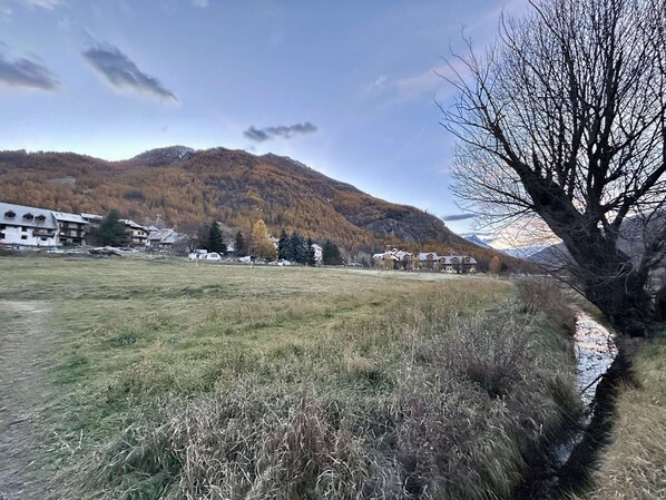 A rural landscape with a mountain in the background, a river, and buildings with traditional architecture. - Cozy Mountain Studio with Balcony, Near Ski Lifts and Shops, Sleeps 4 (La Salle-les-Alpes)