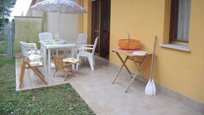 An outdoor patio with a table and chairs, a folding table with a basket, and a small window. - Comfortable Flat Near the sea for six Guests (San Michele al Tagliamento)