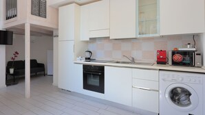 A modern kitchen with white cabinets, a built-in oven, a washing machine, and a coffee maker. - La Cà Fiera 23B. (Bologna)