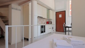 A modern kitchen with white cabinets, a microwave, and a stove. There is a dining area with a table and chairs. A staircase leads to another level. - La Cà Fiera 23B. (Bologna)