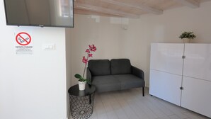 A modern living room with a grey sofa, a white cabinet, a flat-screen TV mounted on the wall, and a potted orchid on a small table. - La Cà Fiera 23B. (Bologna)