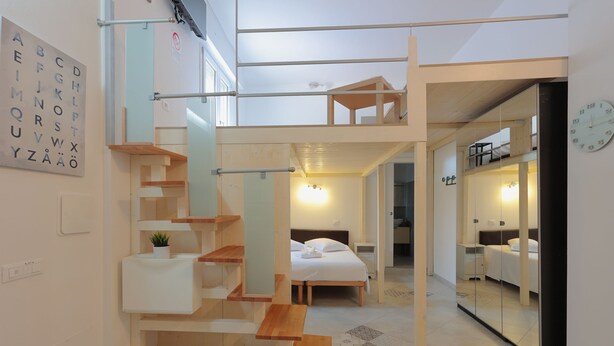 Un interior moderno con un entrepiso, una escalera de madera y un muro espejado que refleja la habitación.