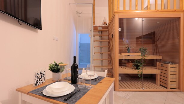 A dining area with a wooden table set for two, a TV mounted on the wall, and a wooden staircase leading to an upper level. - La Cà Fiera 11E. (Bologna)