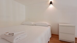 A minimalist hotel room with a neatly made bed, a bedside table, and a wall-mounted light fixture. - La Cà Fiera 11E. (Bologna)