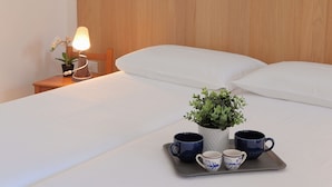 A neatly made bed with white linens, a bedside table with a lamp and a potted plant, and a tray with two mugs and a cup. - La Cà Fiera 11E. (Bologna)
