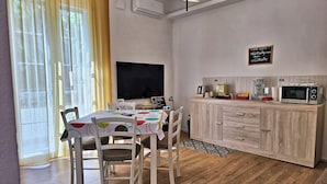 A cozy room with a wooden dining table, chairs, a TV, a kitchenette with a microwave, and a chalkboard on the wall.
