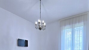 A bedroom with a bed, a desk, a chair, a TV, and a chandelier.