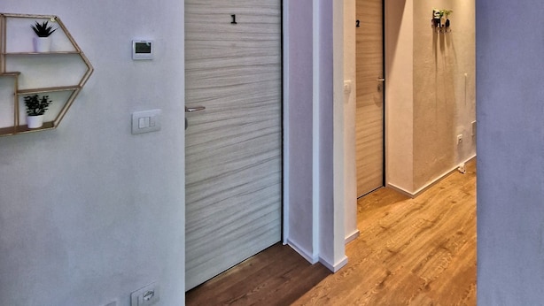 A hallway with a wooden floor, white walls, and a brick archway. There are two doors, one with a number '1' and another with a number '2'.