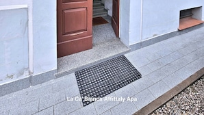 A building entrance with a brown door, a staircase leading inside, and a small window with green shutters.