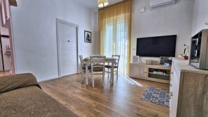 A living room with a wooden floor, a dining table with chairs, a television, and a cabinet.