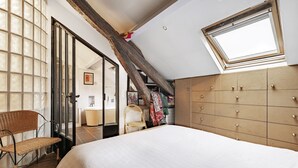 A bedroom with a large bed, a wooden wardrobe, a window, and a chair.