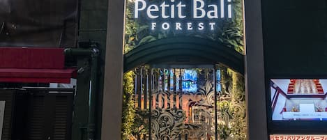 The exterior of Petit Bali Forest Hotel & Resort with a vertical sign, lush greenery, and a decorative entrance.