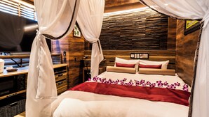 A neatly arranged bed with a red and white bedspread, a wooden headboard, and a television on a wooden stand to the left. - Petit Bali Forest Shinjuku Sanchome (Tokyo)