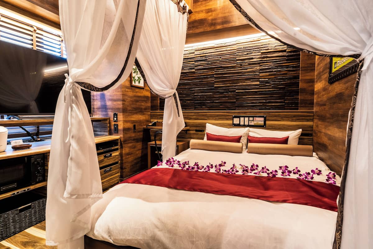 Un lit bien fait, avec une couverture rouge et blanche, une tête de lit en bois et un téléviseur posé sur un meuble en bois, à gauche.